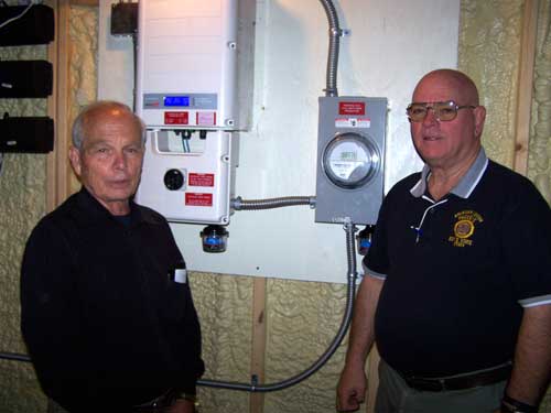 Bill Decker and Bob Schmitt check out the solar inverter in the basement of the Schmitt home that indicates how much energy the solar panels are generating. Toledo Free Press photo by Duane Ramsey